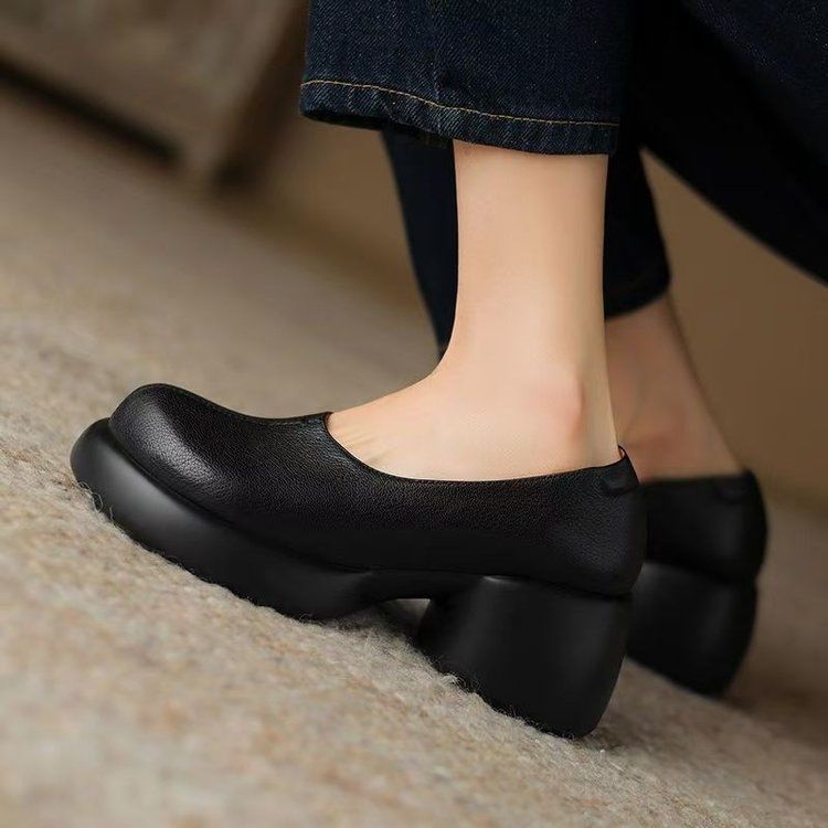 Black PU slip-on pump with rounded sculpted heel and platform sole seen from the front on a beige wool carpet