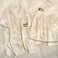 Cream ice silk pajama set with black piping and a panda chest pocket on a white fluffy rug, size M