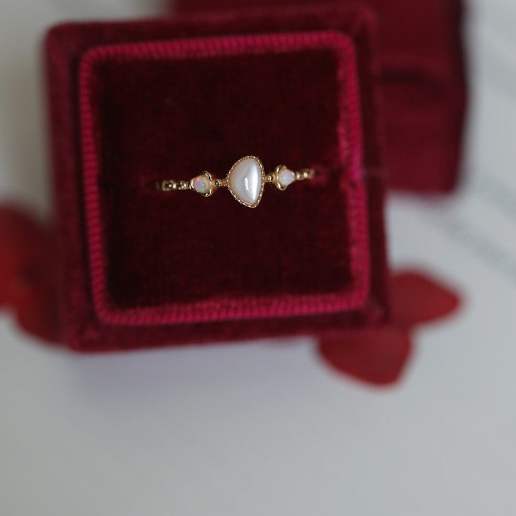 Dainty opal ring set inside a deep red velvet ring box, top view