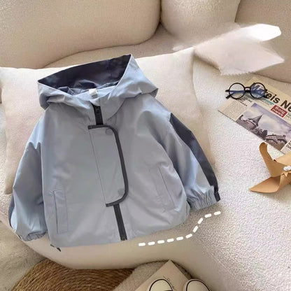 Light blue boys hooded jacket with dark gray sleeve panels, front zipper and side pockets on a cream cushion