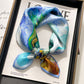 Blue and green abstract printed square scarf with a satin sheen and hemmed edges, shown displayed