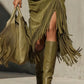 Fringe along the slit and hem of the olive green dress with olive knee high boots and a fringe handbag