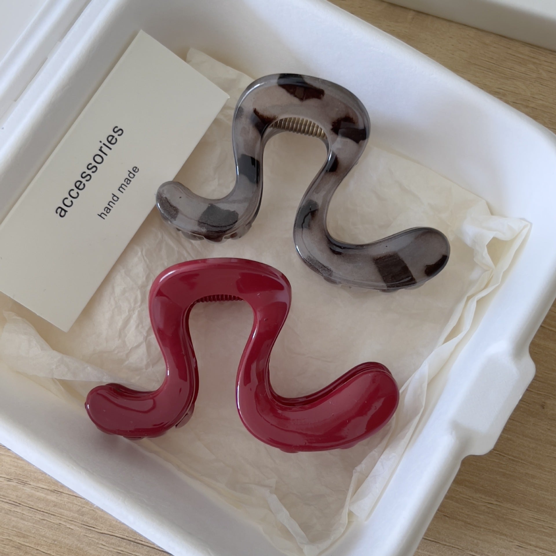 Wine red and smoky grey wavy claw clips displayed together in an open cream gift box