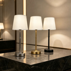 White fabric shade table lamps in gold, silver and black on a dark marble surface