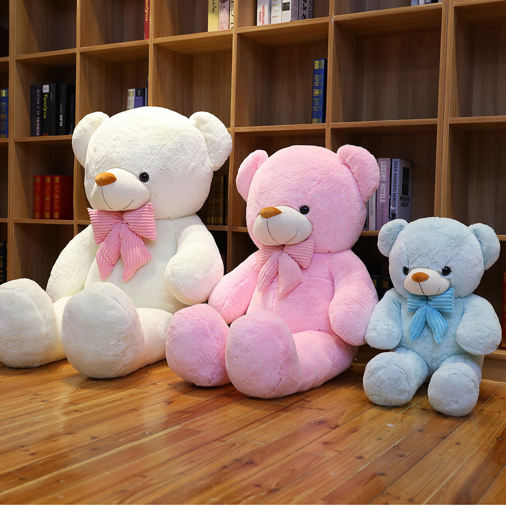 Cream white, pink and light blue plush teddy bears with striped bow ties sitting in a row in front of a bookshelf