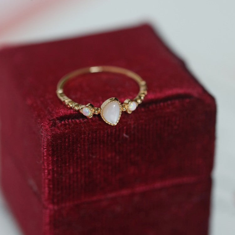 Gold-tone teardrop opal ring resting on the edge of a red velvet ring box
