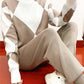 Model in a khaki and white argyle high neck sweater and khaki knit pants sitting on a red floor taking a mirror photo