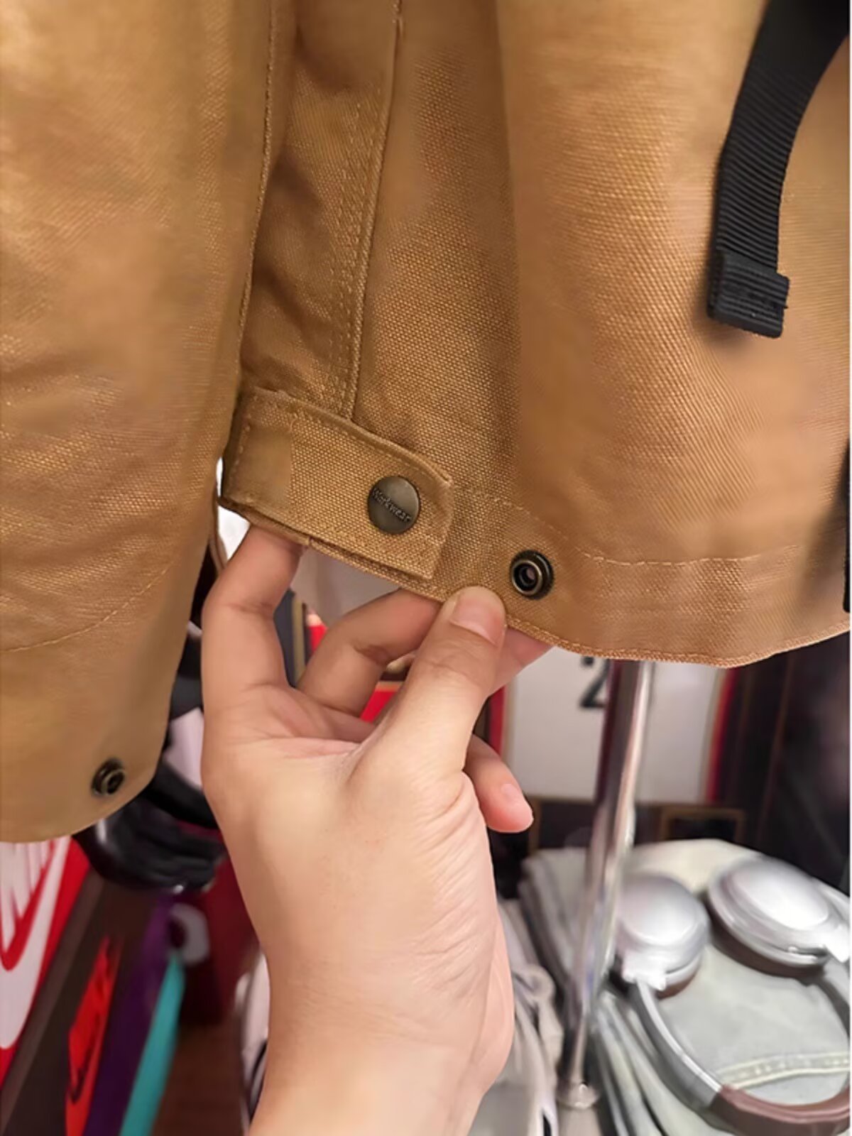 Close view of the khaki jacket hem with a snap-button tab held in a hand