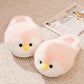 Pink plush penguin slippers with yellow beaks and black eyes on a beige rug beside a newspaper