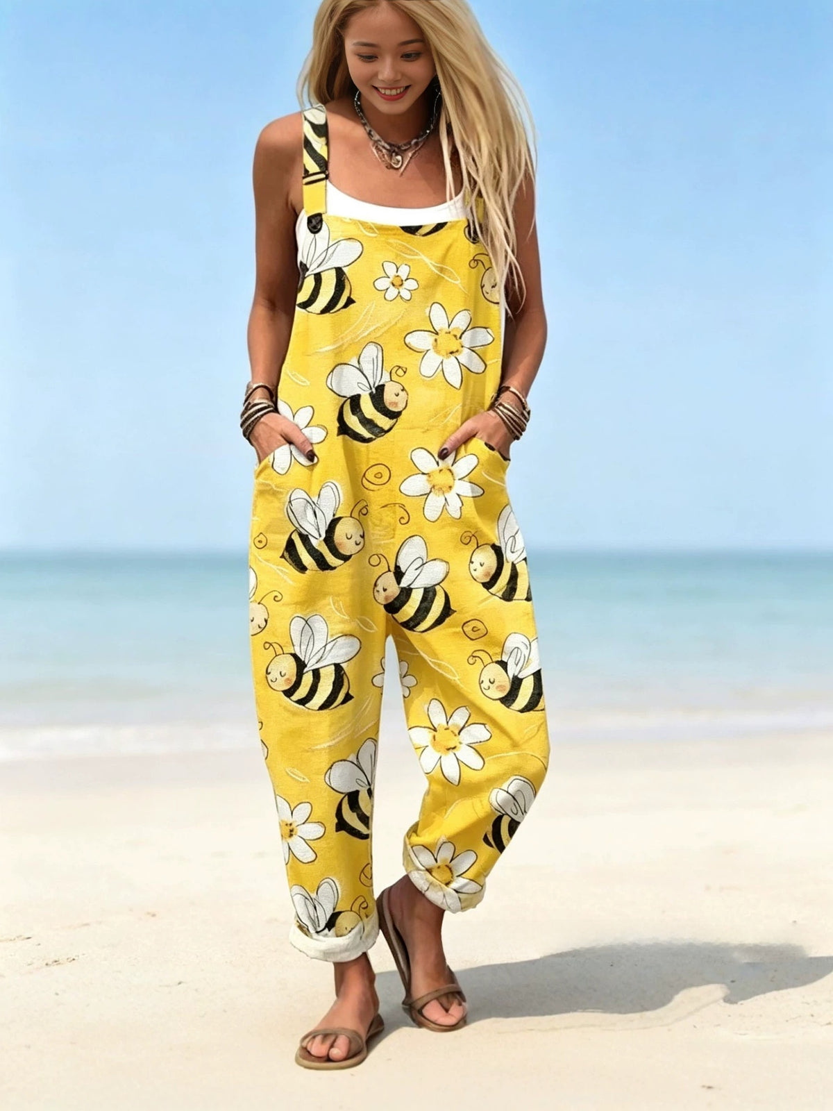 Woman in yellow overalls with a bee and daisy print, loose cuffed legs and front pockets on a beach