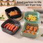 Four silicone air fryer liner trays in black, teal, gray and green holding wings, fries and sausages