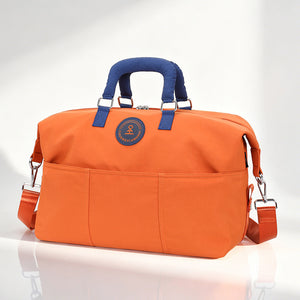 Orange duffel travel bag with navy blue padded handles, front slip pockets and a detachable shoulder strap, studio view