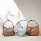 Three crescent leather bags in taupe, pale blue and caramel brown standing on a pale green surface