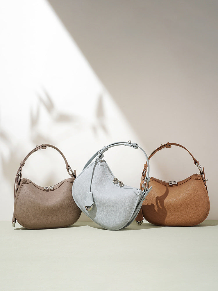 Three crescent leather bags in taupe, pale blue and caramel brown standing on a pale green surface