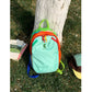 Mint color block travel backpack resting on grass, rainbow contrast trim and contrast shoulder straps