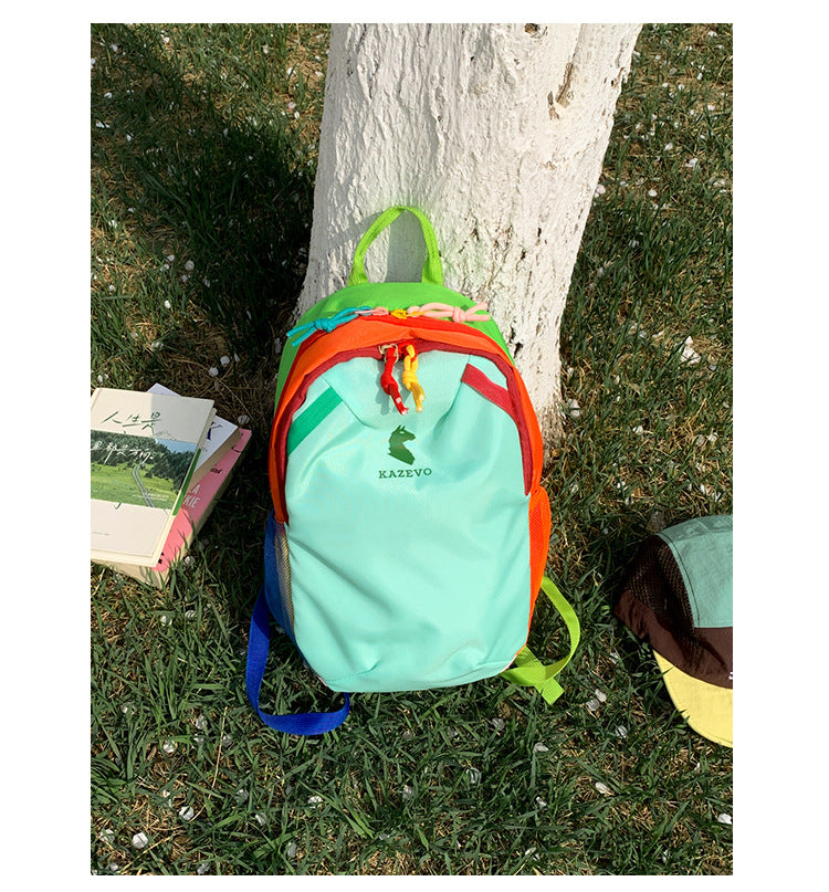 Mint color block travel backpack resting on grass, rainbow contrast trim and contrast shoulder straps