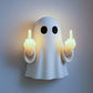 Close view of the ghost wall night light glowing warm with both hands raised on a grey wall