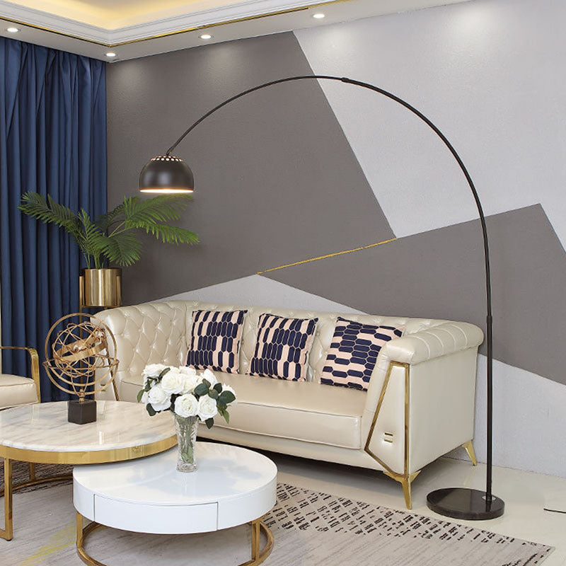 Metal dome shade of an arc floor lamp lit warm above a living room seat