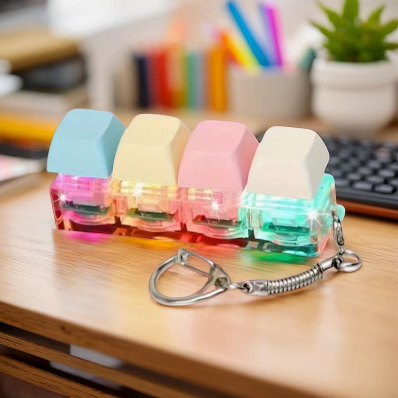Pastel keycap fidget clicker keychain resting on a wooden desk beside a laptop