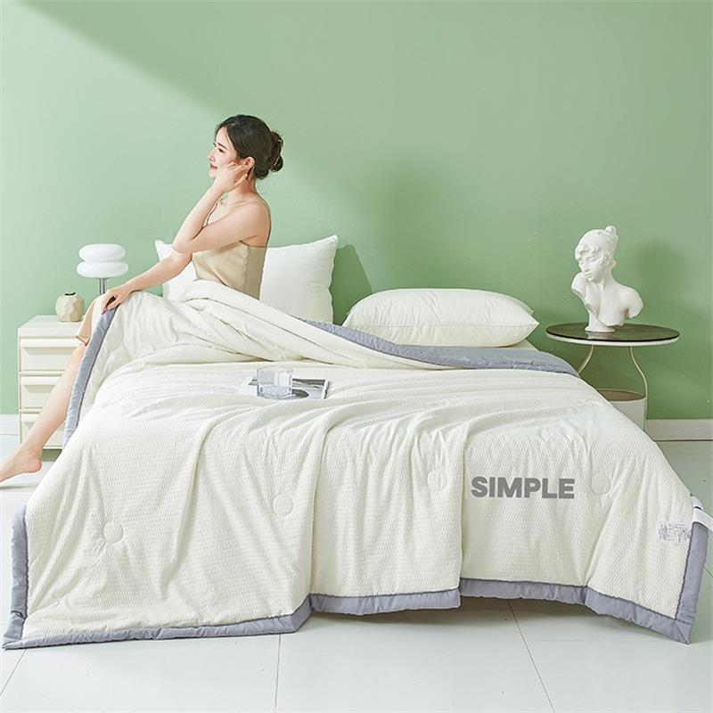 White seersucker summer cooling quilt with a colored border draped on a styled bed