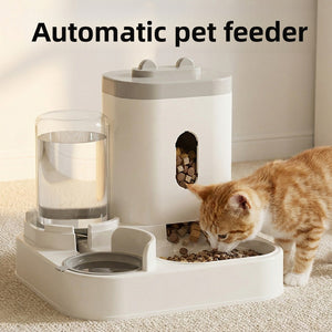 White plastic gravity pet feeder and water dispenser with a ginger cat eating kibble from the twin bowl base