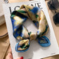 Navy blue and green floral printed square scarf with a satin sheen and hemmed edges, shown displayed