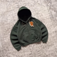 Green boxy zip-up hoodie with front pocket and ribbed cuffs lying on a patterned rug with a tiger embroidery
