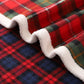 Red, green and navy tartan blanket rippling over its cream pile reverse in a close up
