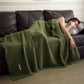 Olive Green cotton gauze throw blanket with tassel fringe, draped over a woman asleep on a dark sofa, view 4 of 4