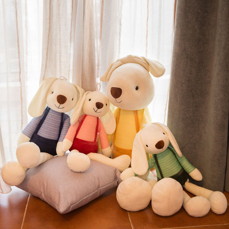 Four plush rabbits in blue, coral, yellow and mint outfits sitting together by a window with curtains