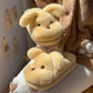 Yellow puppy plush house slipper with floppy ears on a cushion beside a second slipper held in the air