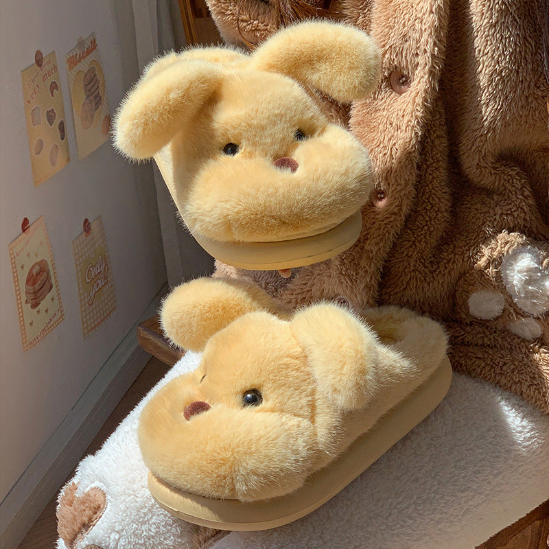 Yellow puppy plush house slipper with floppy ears on a cushion beside a second slipper held in the air