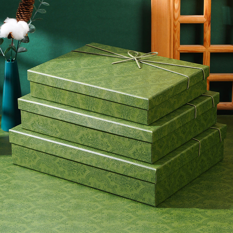 Stack of three olive green damask-pattern gift boxes with cord bows tied on the lids