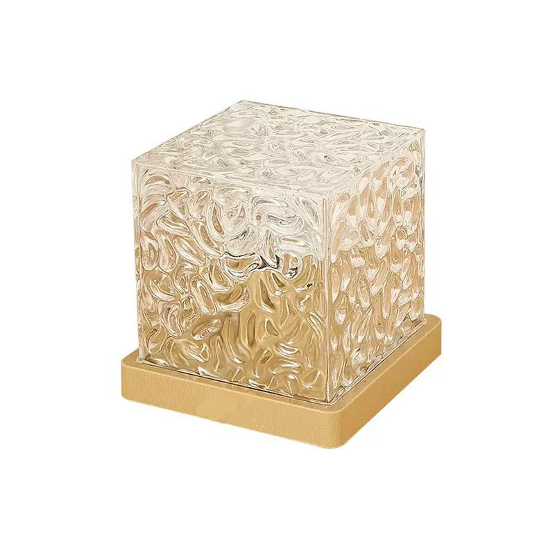 Clear rippled cube water ripple lamp switched off, resting on a square gold tone base