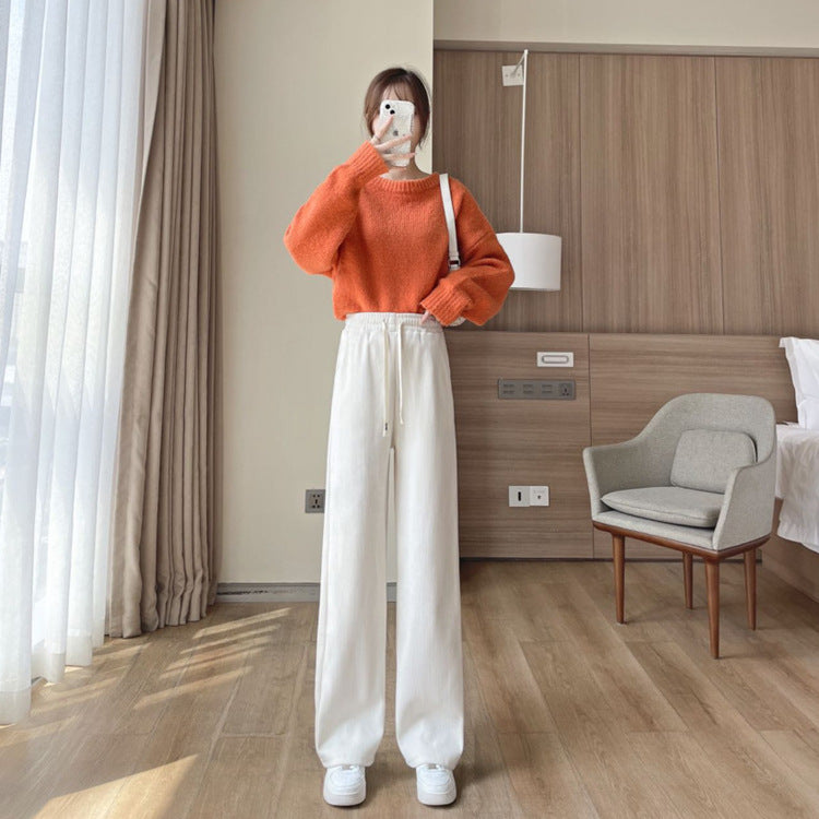 Cream wide-leg drawstring pants worn with an orange sweater and white sneakers in a bedroom