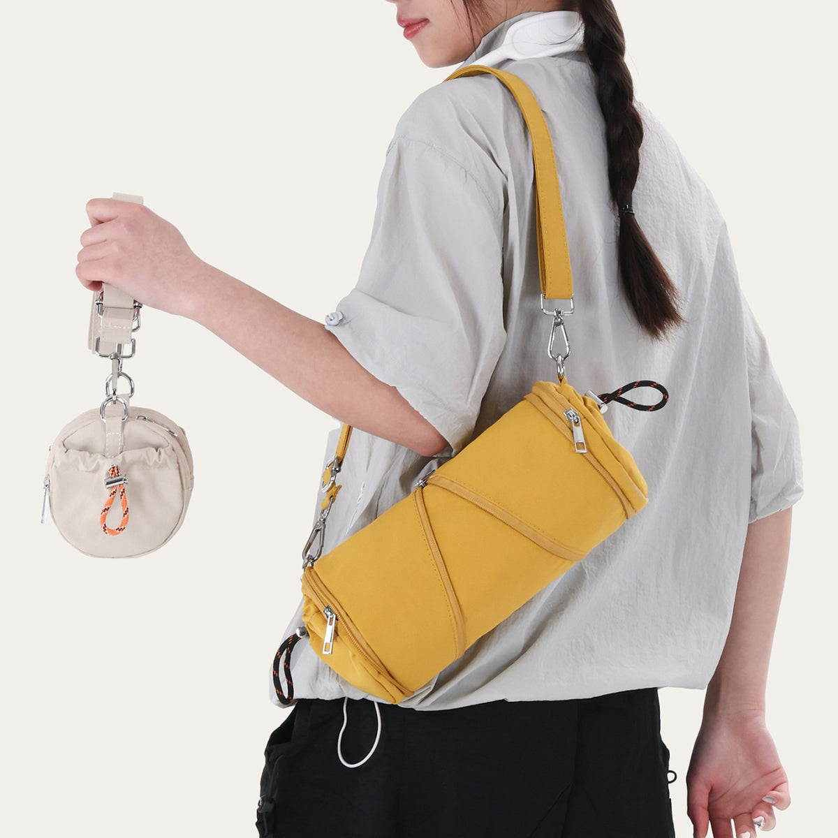 Woman carrying a mustard yellow cylindrical nylon shoulder bag with a small cream pouch hanging from the strap