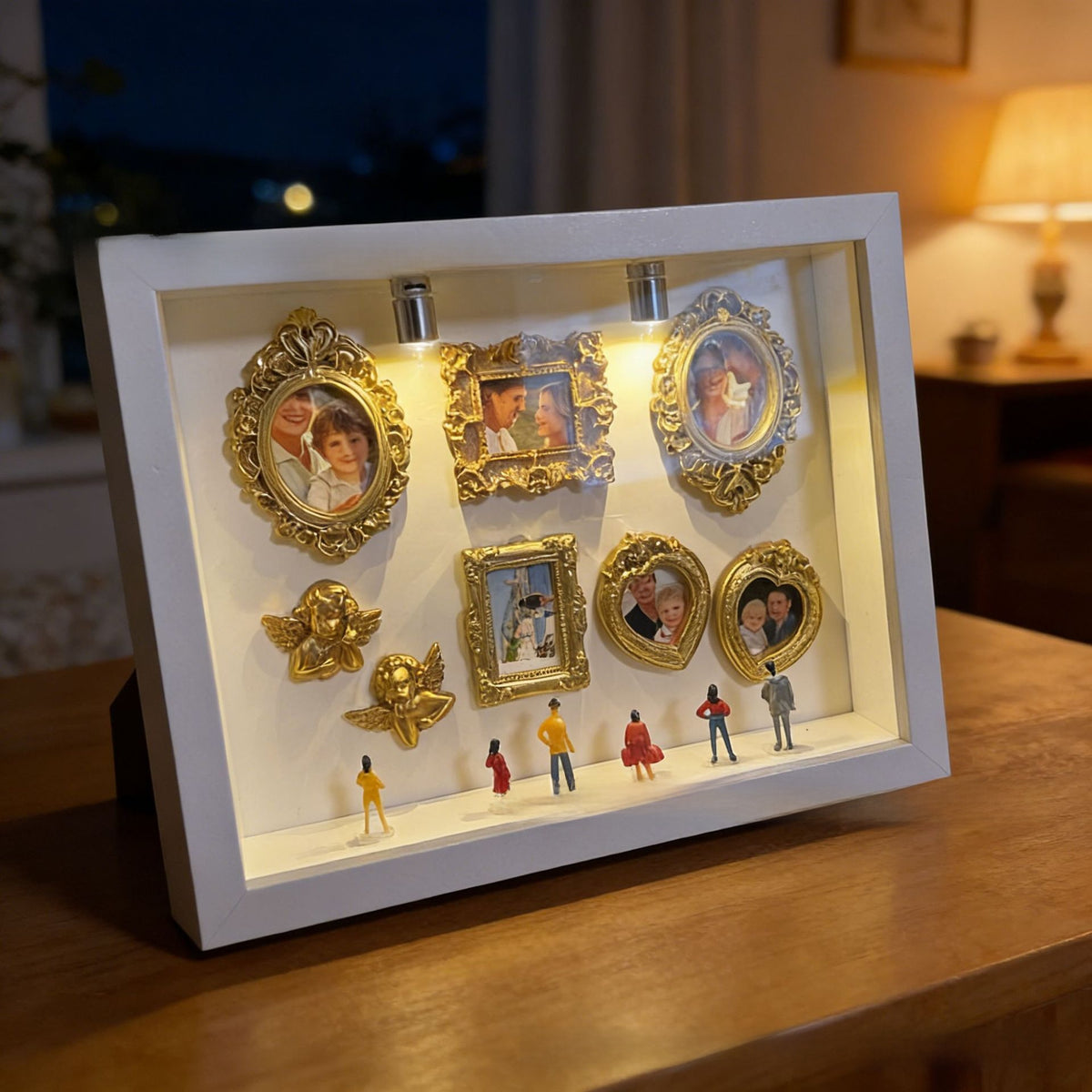 White shadow box set with gold mini photo frames, cherubs and figurines glowing on a wooden table in the evening