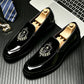 Glossy black loafers with a black velvet vamp and an embroidered laurel crest on a desk with a tie, size 40 option