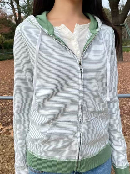 Woman wearing a green striped zip-up hoodie with white drawstrings over a white henley top, front view