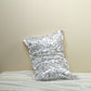 White silk pillowcase printed with black line-drawn camellia blooms, leaning on a cream wall above white silk