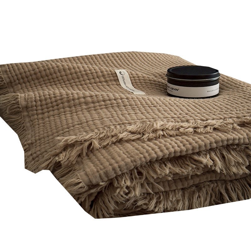 Tan cotton gauze blanket folded with a black jar on top, close view of the waffle weave and fringed edge