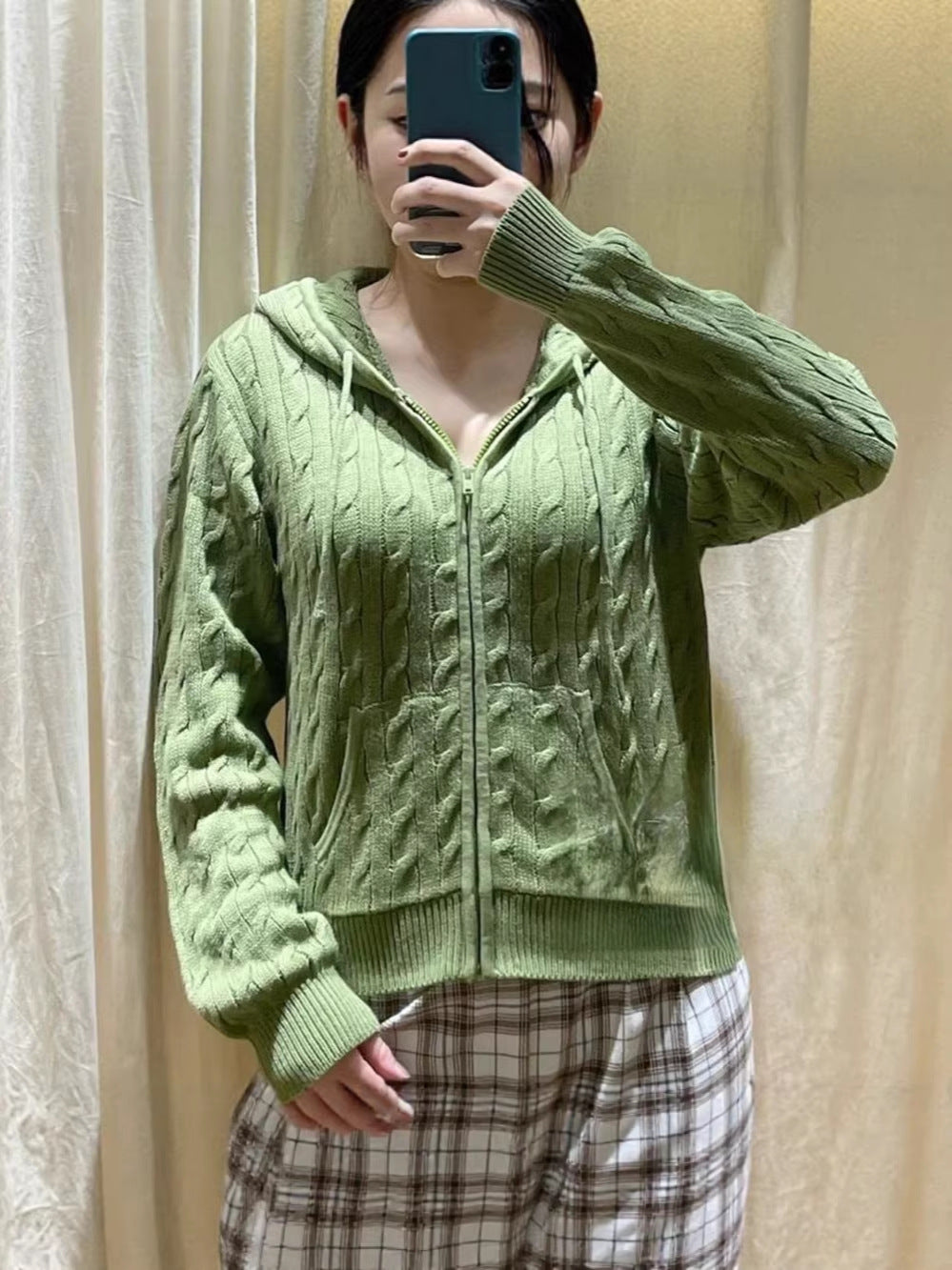 Woman wearing avocado green cable knit zip hooded cardigan over a plaid skirt, front view