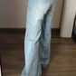 Back view of light wash flared jeans with a curved back pocket and a mint colored patch at the waistband