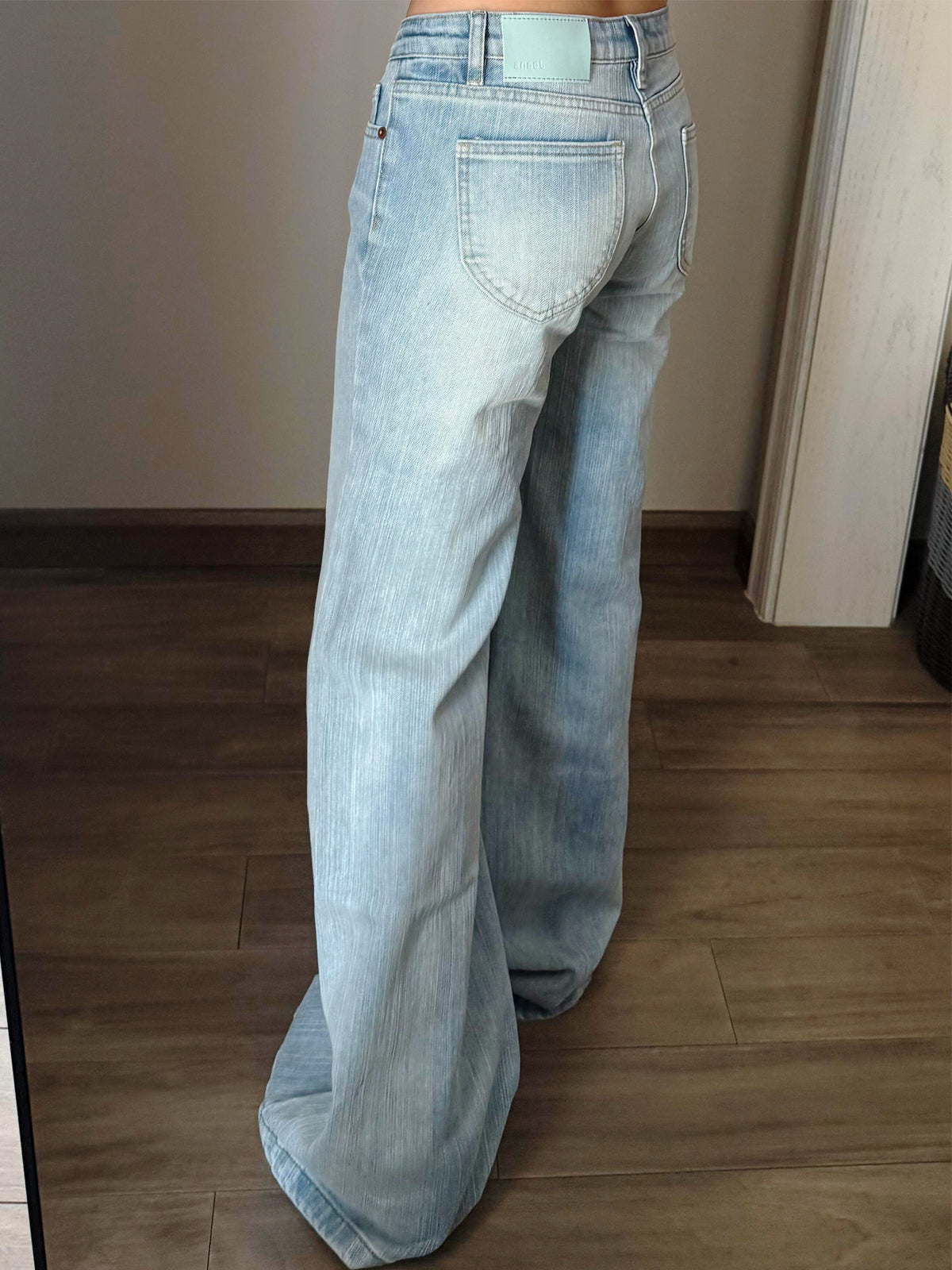 Back view of light wash flared jeans with a curved back pocket and a mint colored patch at the waistband