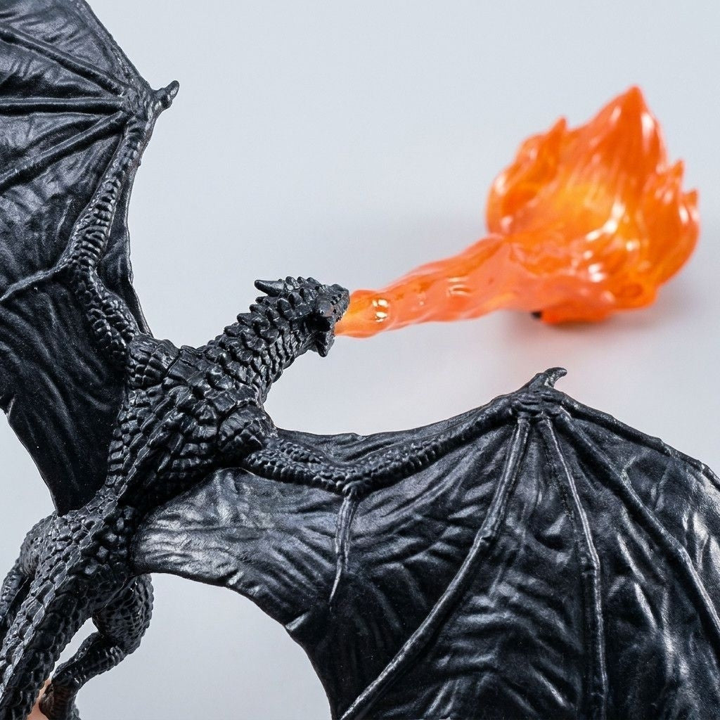 Close-up of the black textured dragon with spread wings breathing a translucent orange flame on a pale background