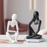 White and black abstract resin meditator figurines seated in thinking poses on a bright tabletop