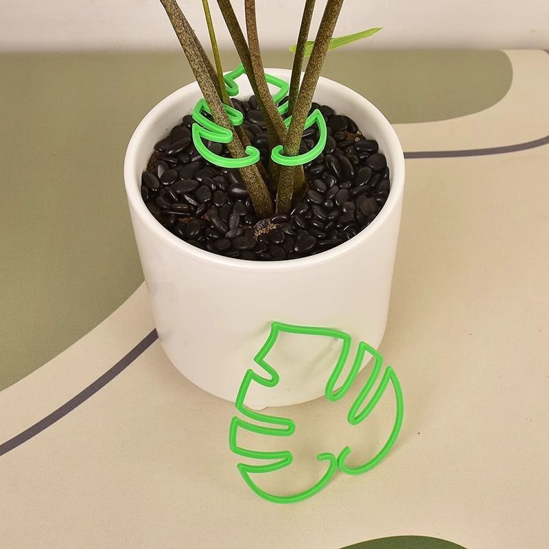 Green monstera leaf plant clip around stems in a white pot, with a second green leaf clip beside the pot