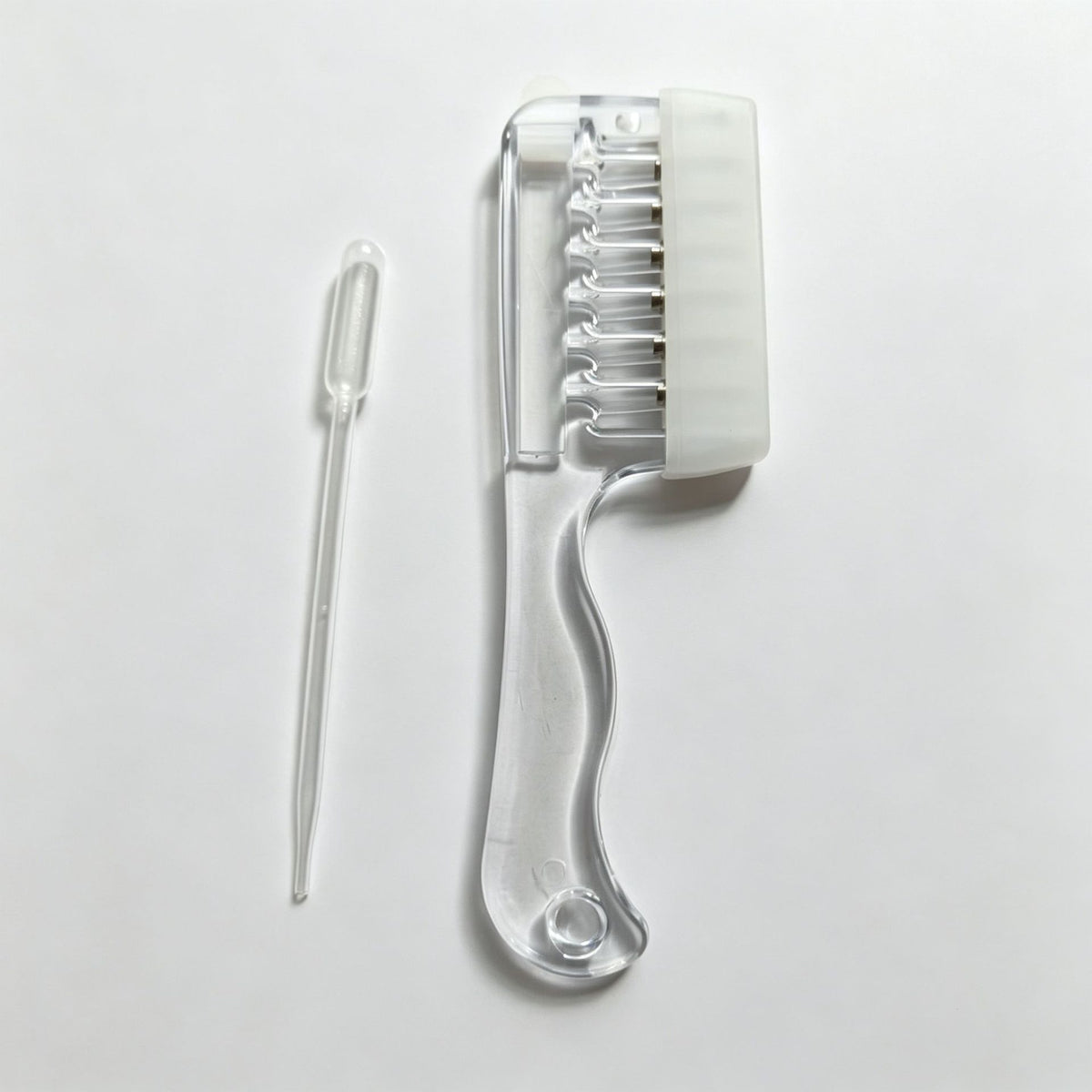 Transparent white scalp liquid comb with white soft rubber cover and a dropper pipette on a light surface, OPP bag option