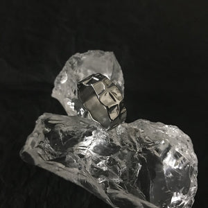 Textured steel band resting on clear quartz against black, hollows holding shadow and ridges catching light