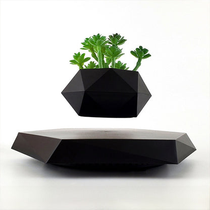 Black faceted pot with a green artificial succulent floating above a levitation base on white